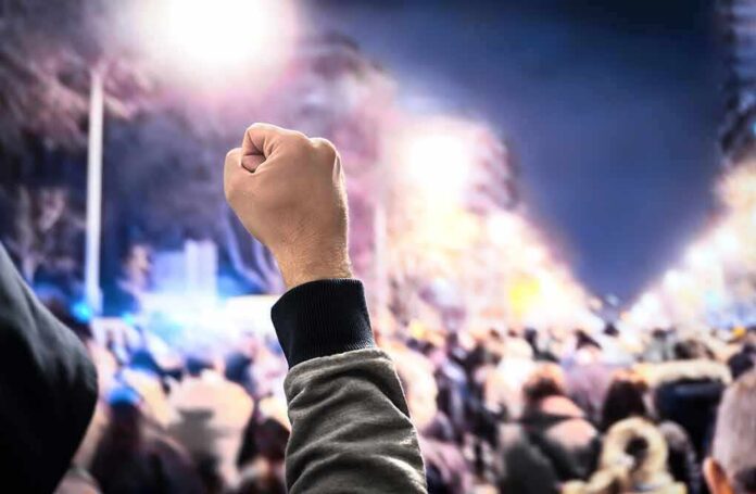 shutterstock_1227767953 Raised fist in front of a large crowd at night