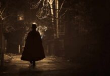 Silhouette of a person in a long coat and hat walking down a dimly lit alley