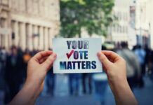 Hands holding a sign about voting in a busy city street
