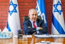 Election Crunch: Netanyahu Seeks Trump Megaphone man in suit seated at a desk with Israeli flags behind him