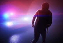 silhouetted person in front of police car with flashing lights