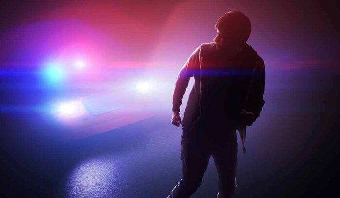 shutterstock_1620882688-1 silhouetted person in front of police car with flashing lights