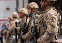 Soldiers in camouflage gear stand in formation holding rifles