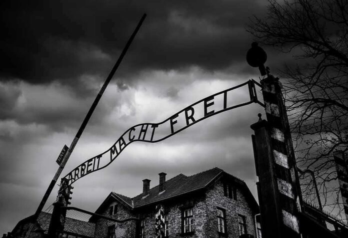 Entrance gate with wrought-iron sign at a historic brick complex under stormy skies