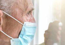 Older man wearing a surgical mask looking out a window