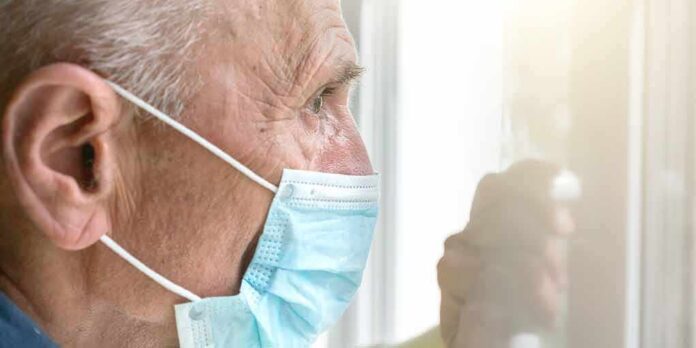 Older man wearing a surgical mask looking out a window