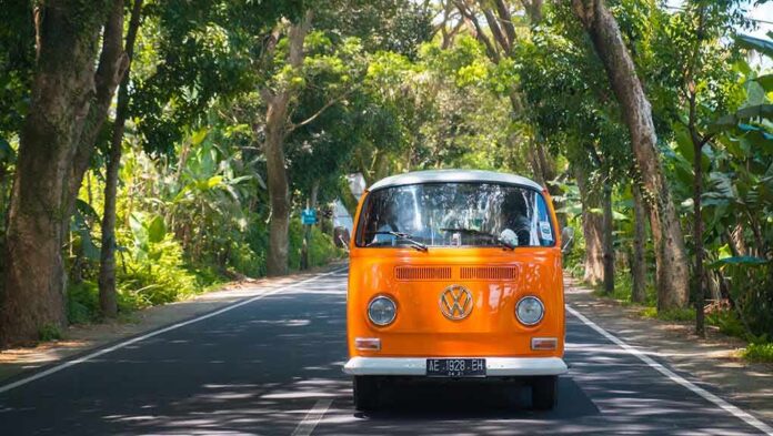 shutterstock_672642379 Orange vintage van driving on a tree-lined road
