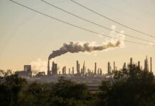Industrial refinery with smokestack emitting plume at sunset