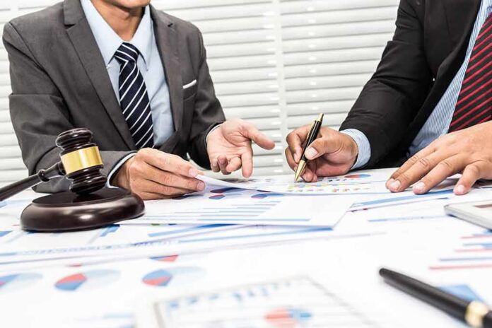 shutterstock_790231258 Two businesspeople in suits reviewing charts at a desk with a gavel